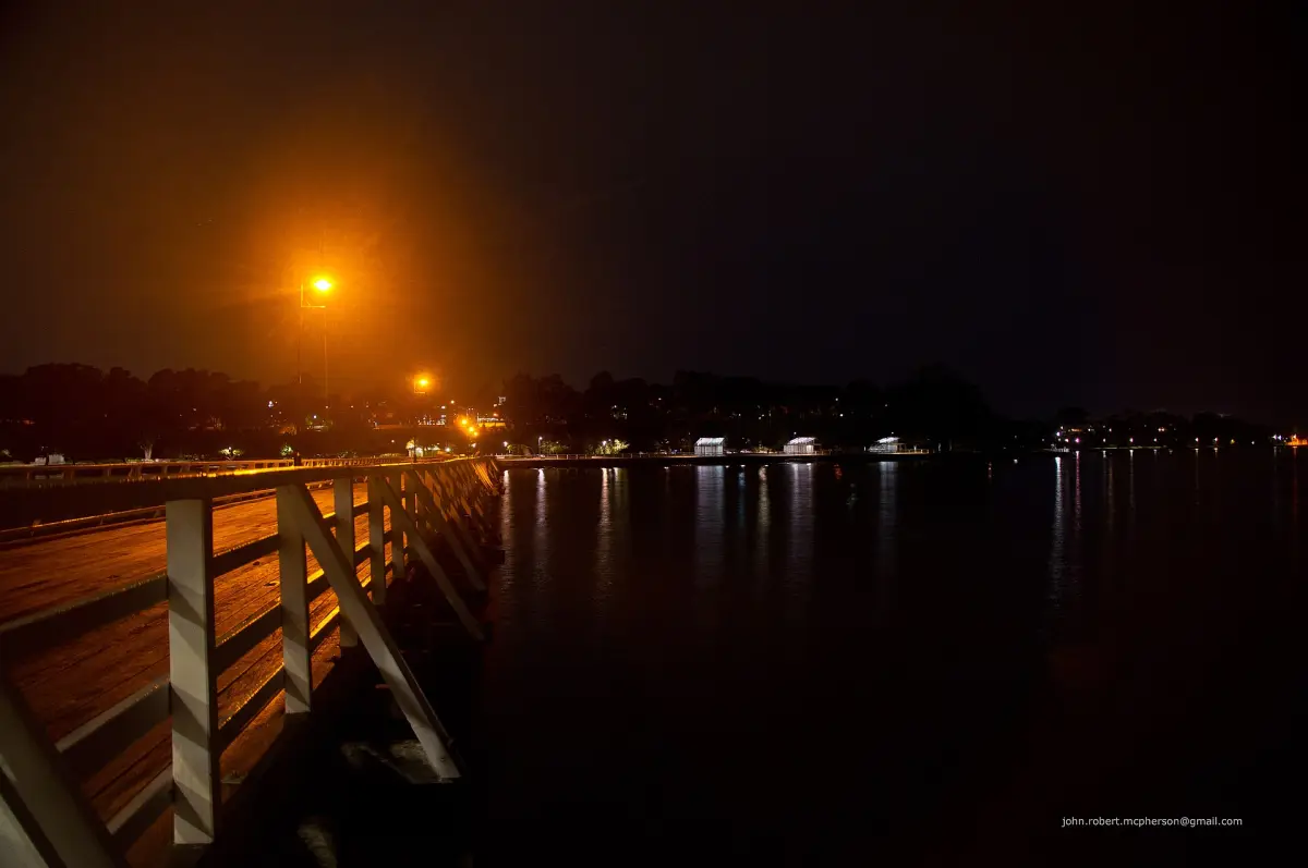 Waterfront boardwalk at night with lights reflecting on the water