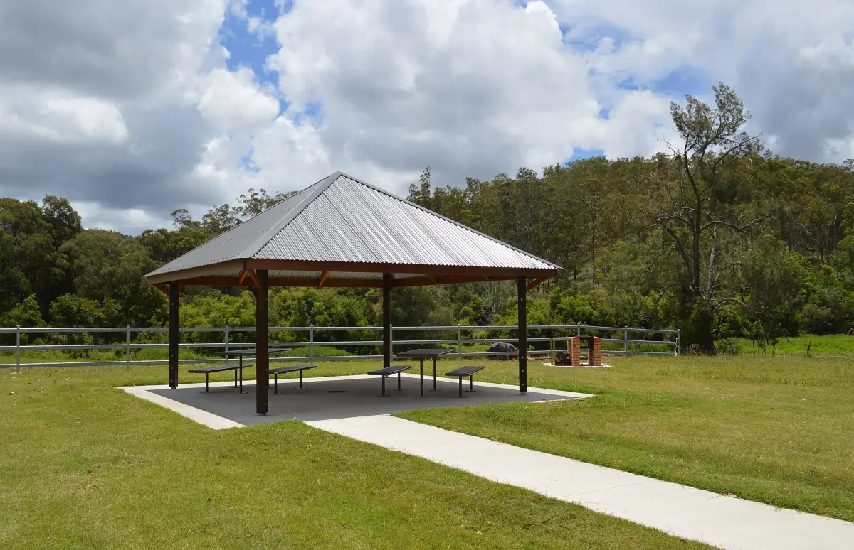 Park picnic shelter on a concrete pad with a path across mown grass